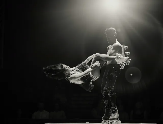 Foto en blanco y negro de Maikel Mota girando a su compañera sobre patines bajo un foco